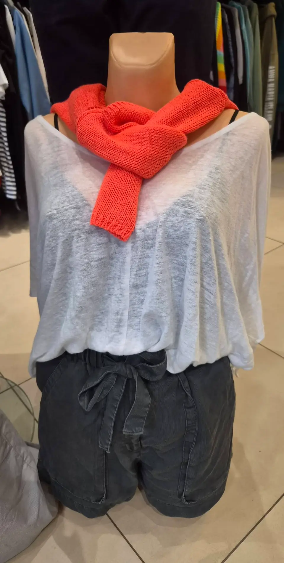 Ein weißes Leinenoberteil mit korallenrotem Pullover über den Schultern und graue Shorts